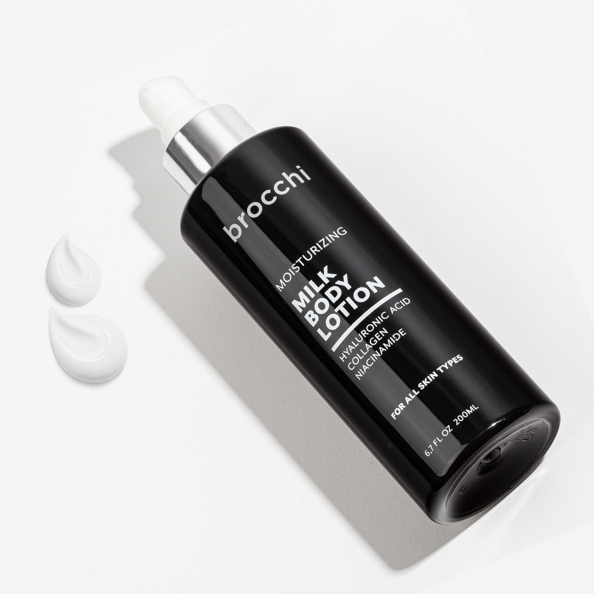 Milk Body Lotion bottle lying beside drops of lotion